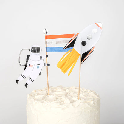 Cake toppers featuring a spaceman with a flag and a rocket blasting off on a frosted cake.