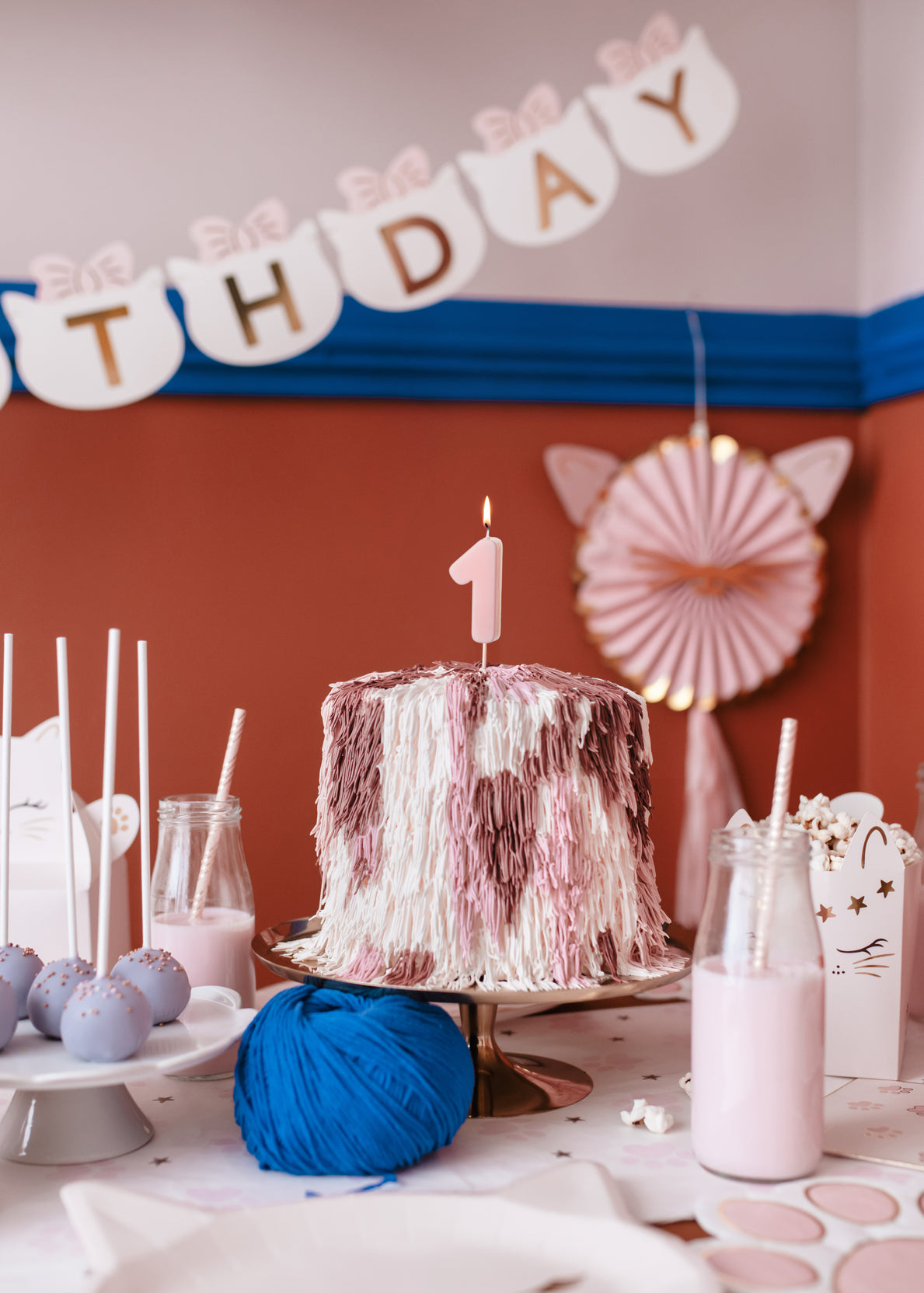 baby pink number 1 birthday candle on a cake surrounded by cat themed party supplies 