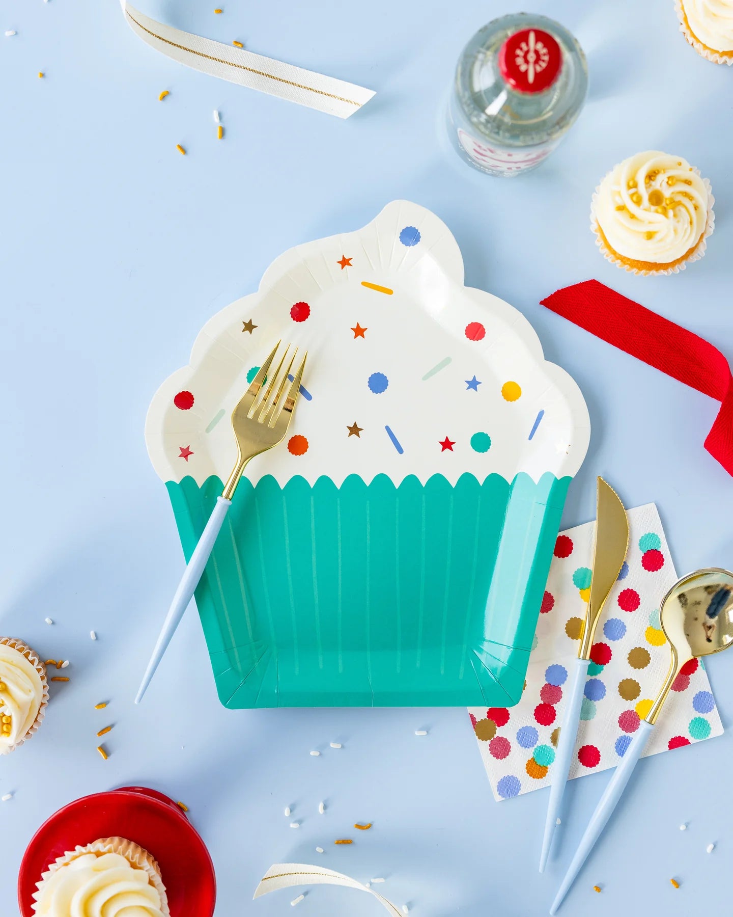 a birthday party table with a cupcake shaped paper plate, napkin with a sprinkle design and blue and gold plastic cutlery