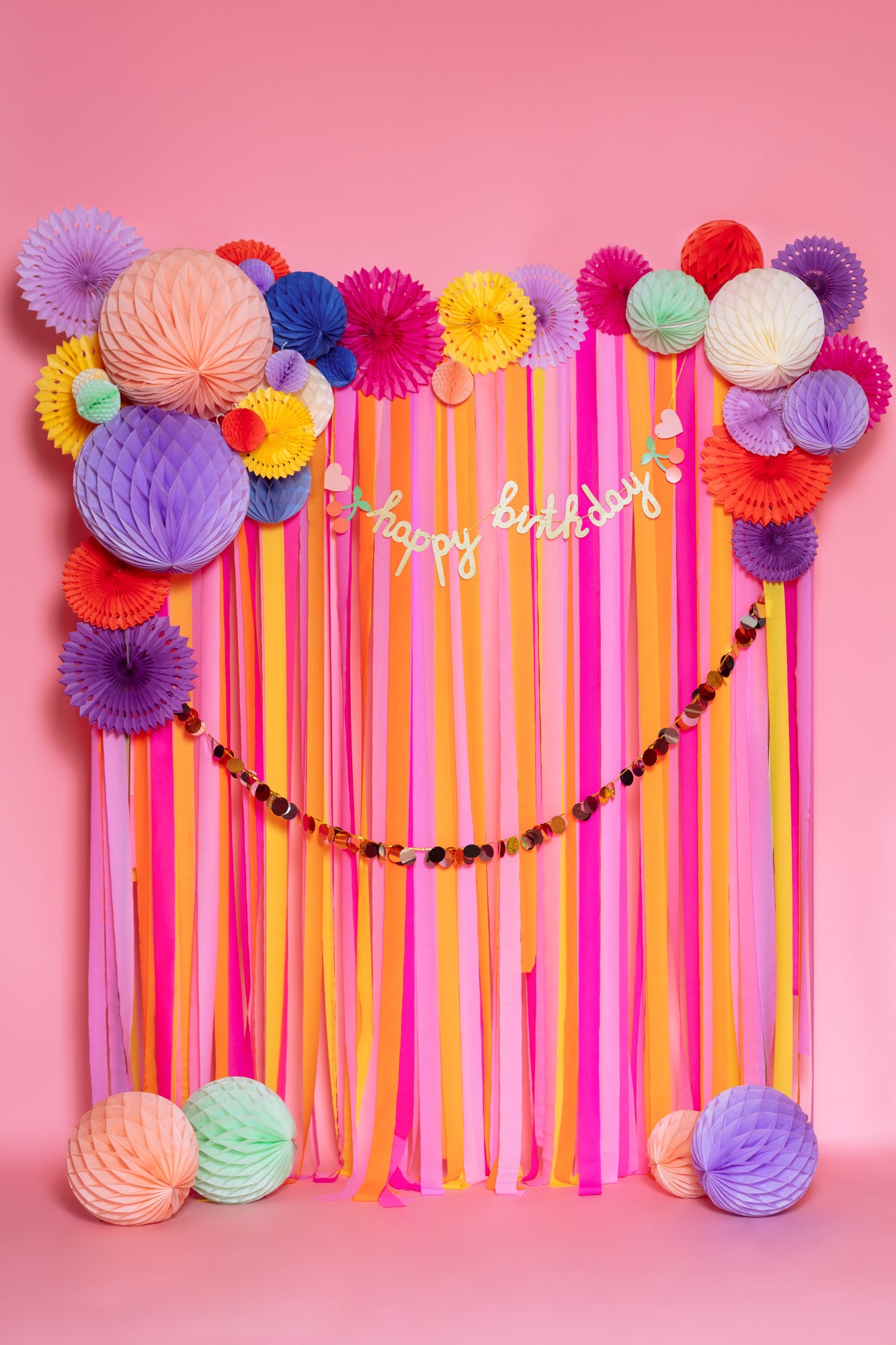 happy birthday backdrop with hanging streamers, honey combs and paper fans in bright and bold colours