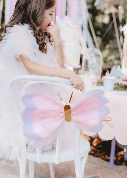 girl sitting on a chair with a paper butterfly attached to the back of her chair 