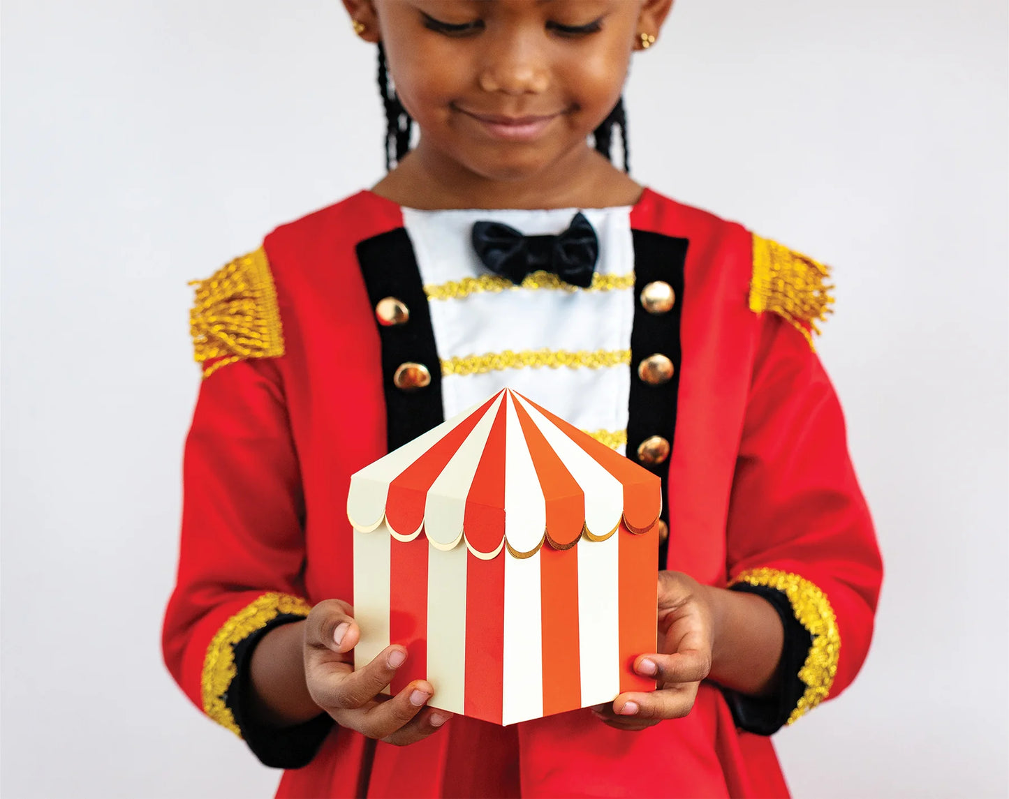 little child in carnival costume holding a closed carnival tent treat box