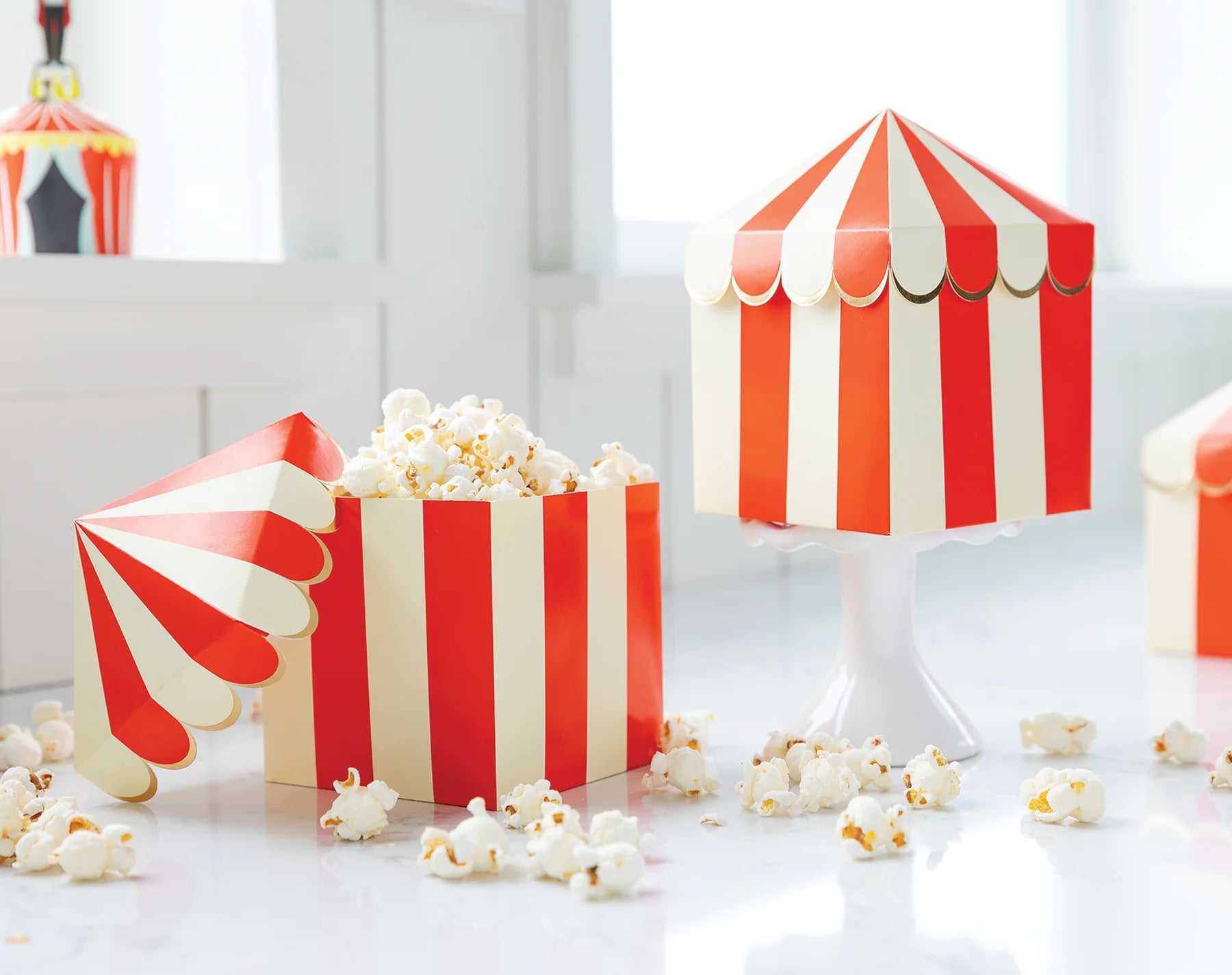 Two carnival tent treat boxes: one open with overflowing popcorn, the other closed.