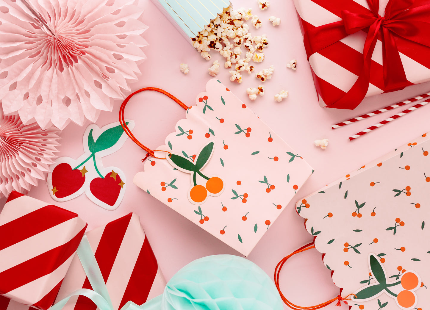 pink table with wrapped presents, cherry gift bag, paper fans and a popcorn treat box