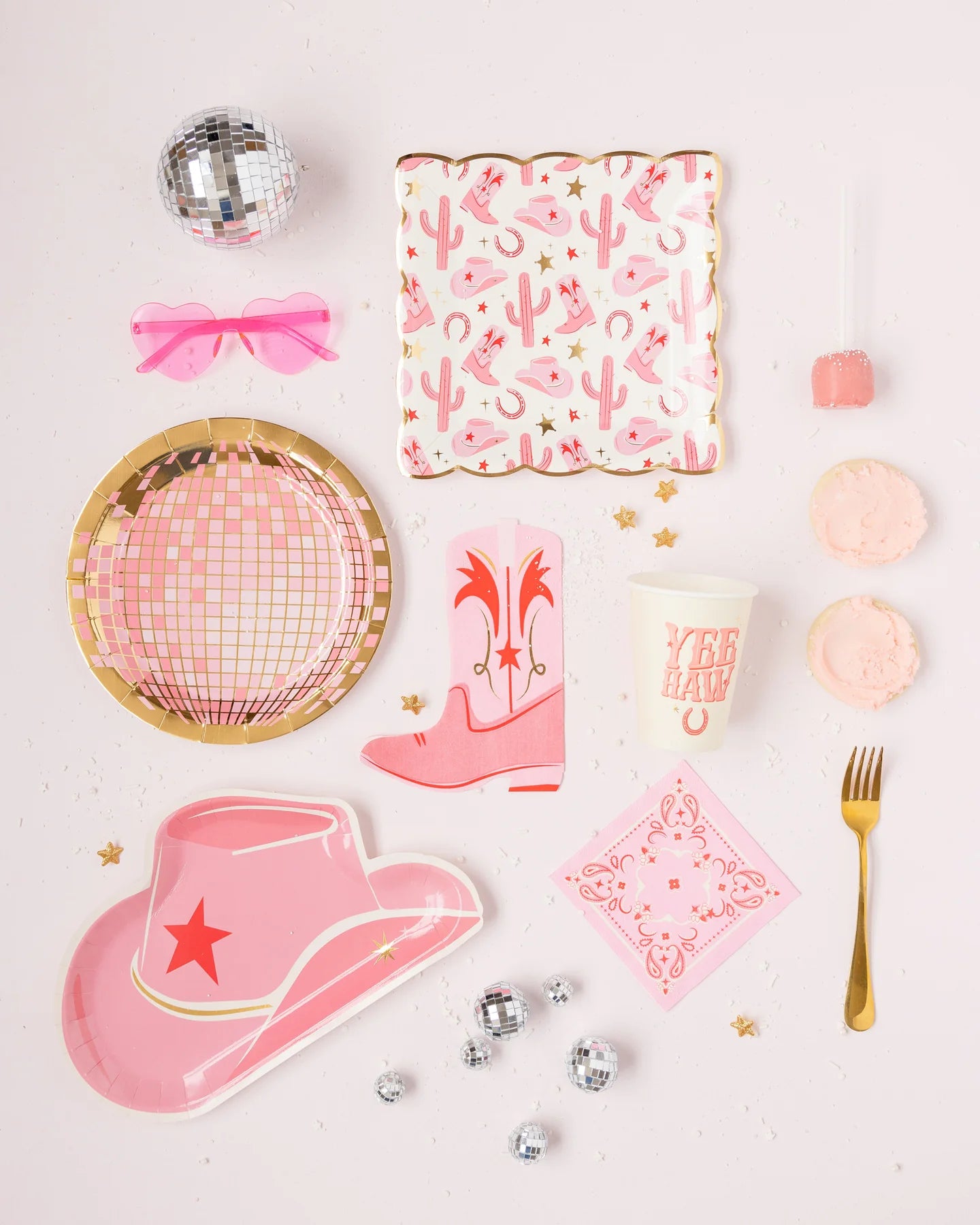 flat lay of pink Western-themed party decor with a cowboy hat paper plate, boot shaped napkin and disco ball plate