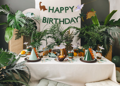 full dino party deco including banner, table settings, party hats and drink sleeves