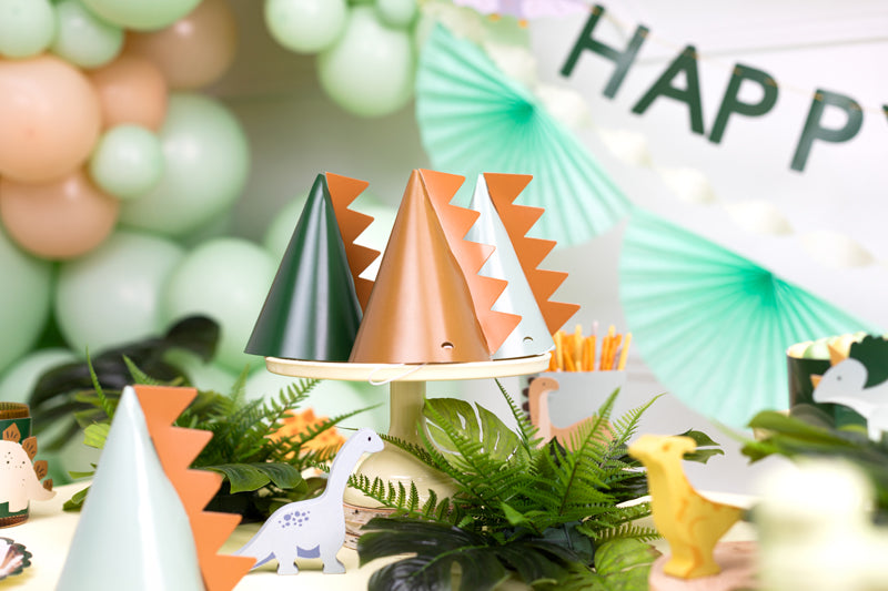 dinosaur table setup with party hats displayed on a cake stand