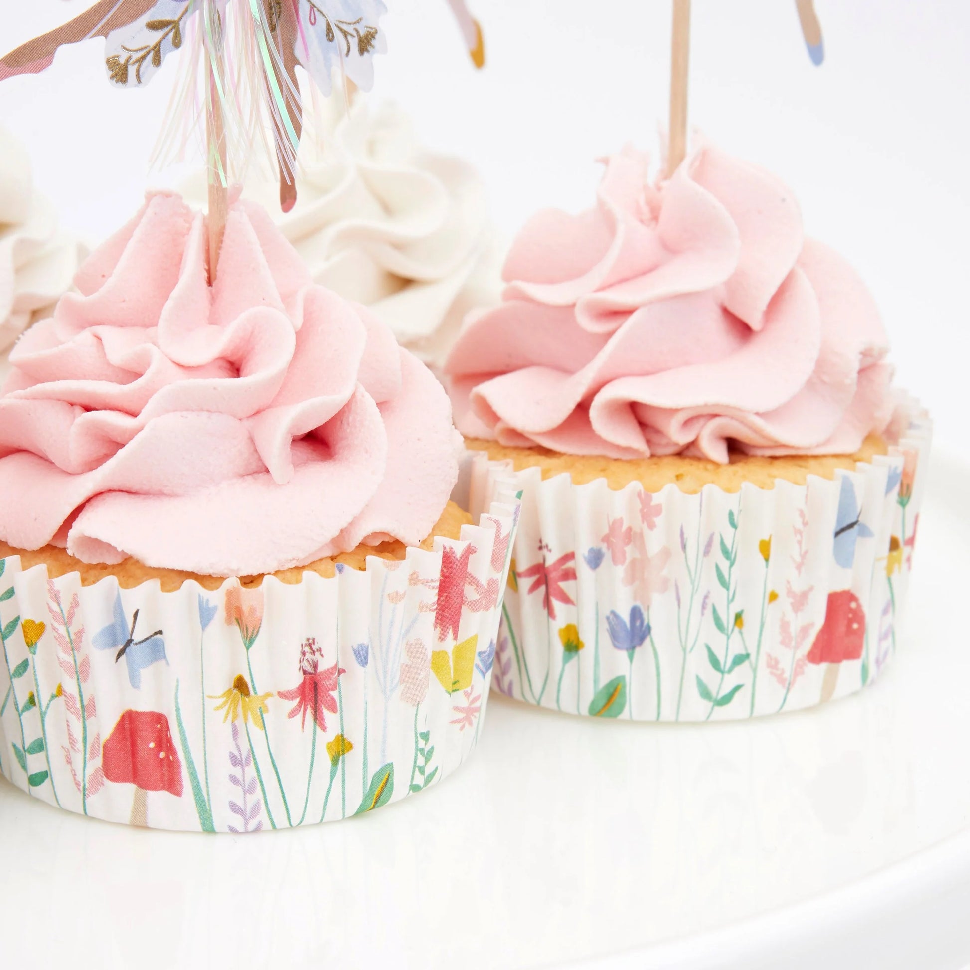 2 cupcakes on a tray with floral cupcake wrappers and pink frosting.