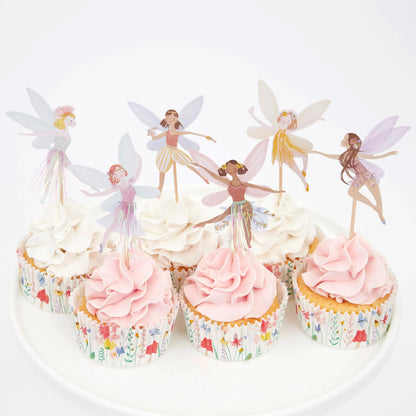 A plate with cupcakes and fairy cupcake toppers on it.