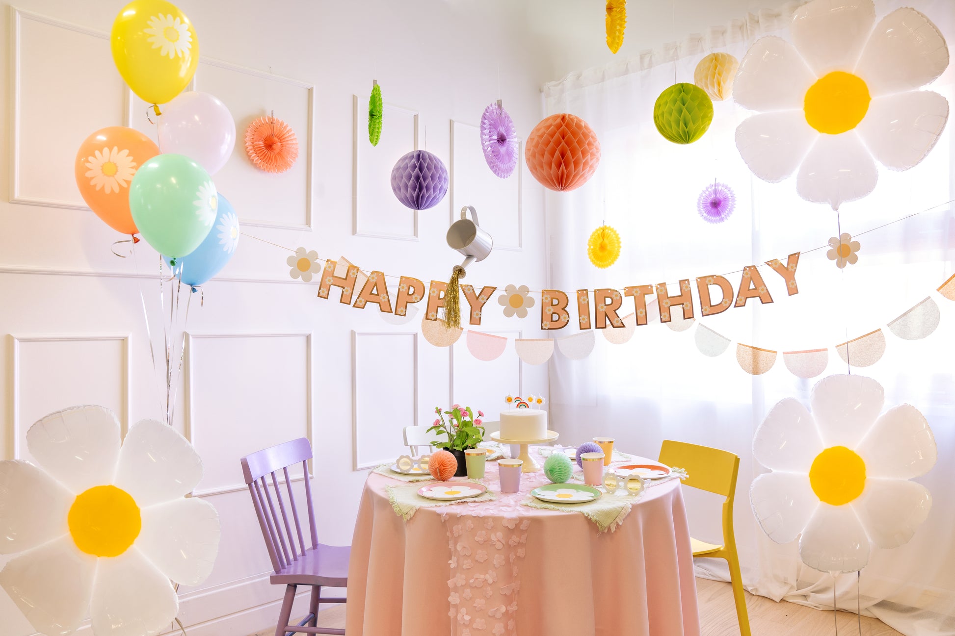 Colorful groovy-themed birthday setup featuring a daisy banner and fun decor, including balloons and hanging honeycombs.