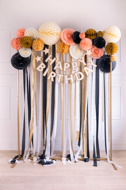 Birthday display with honeycombs, paper fans, and streamers in beige, peach, black, and gold.