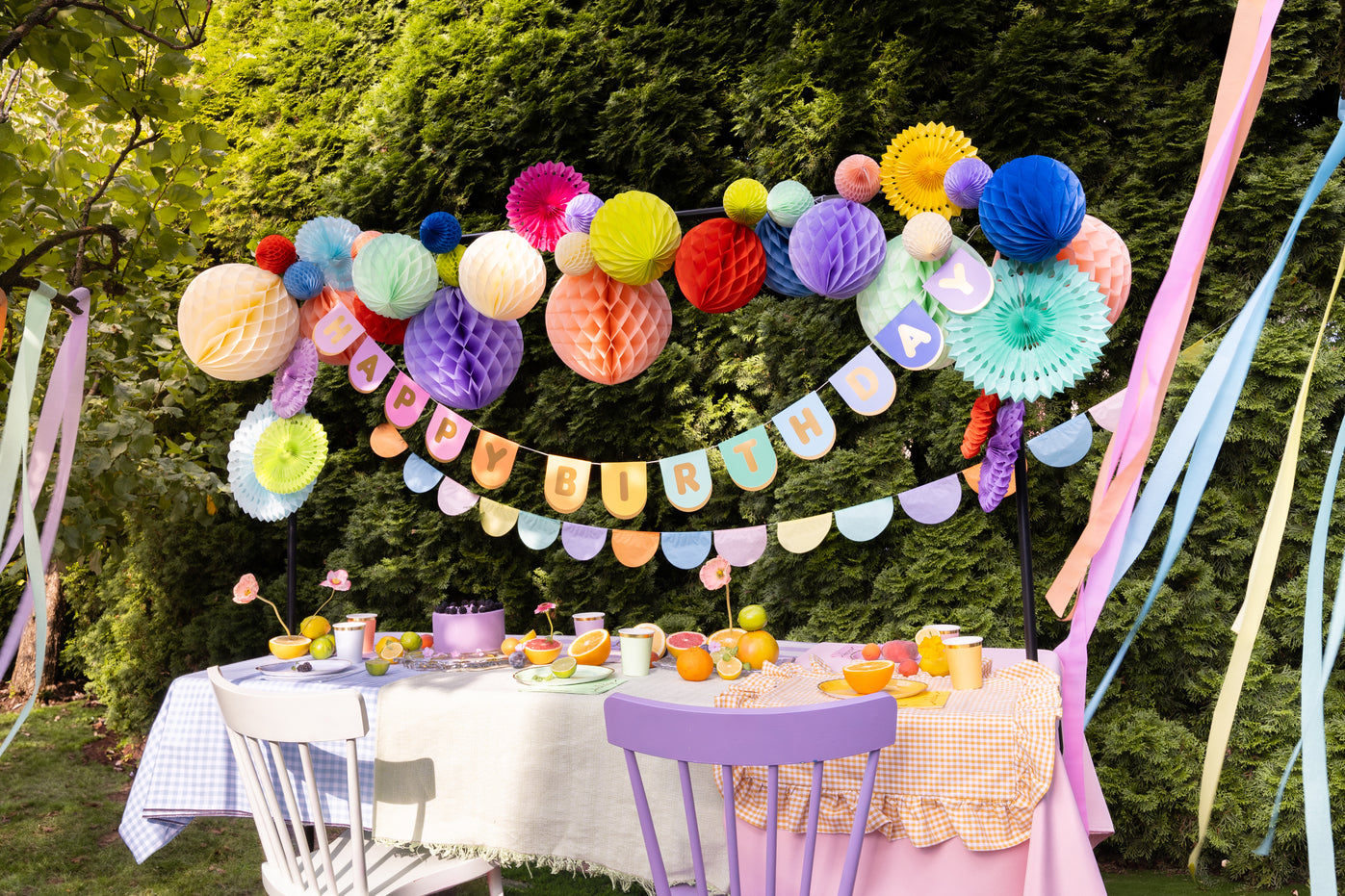 Outdoor birthday setup featuring colourful decor, including streamers, "Happy Birthday" banners, and honeycomb and rosette decorations.