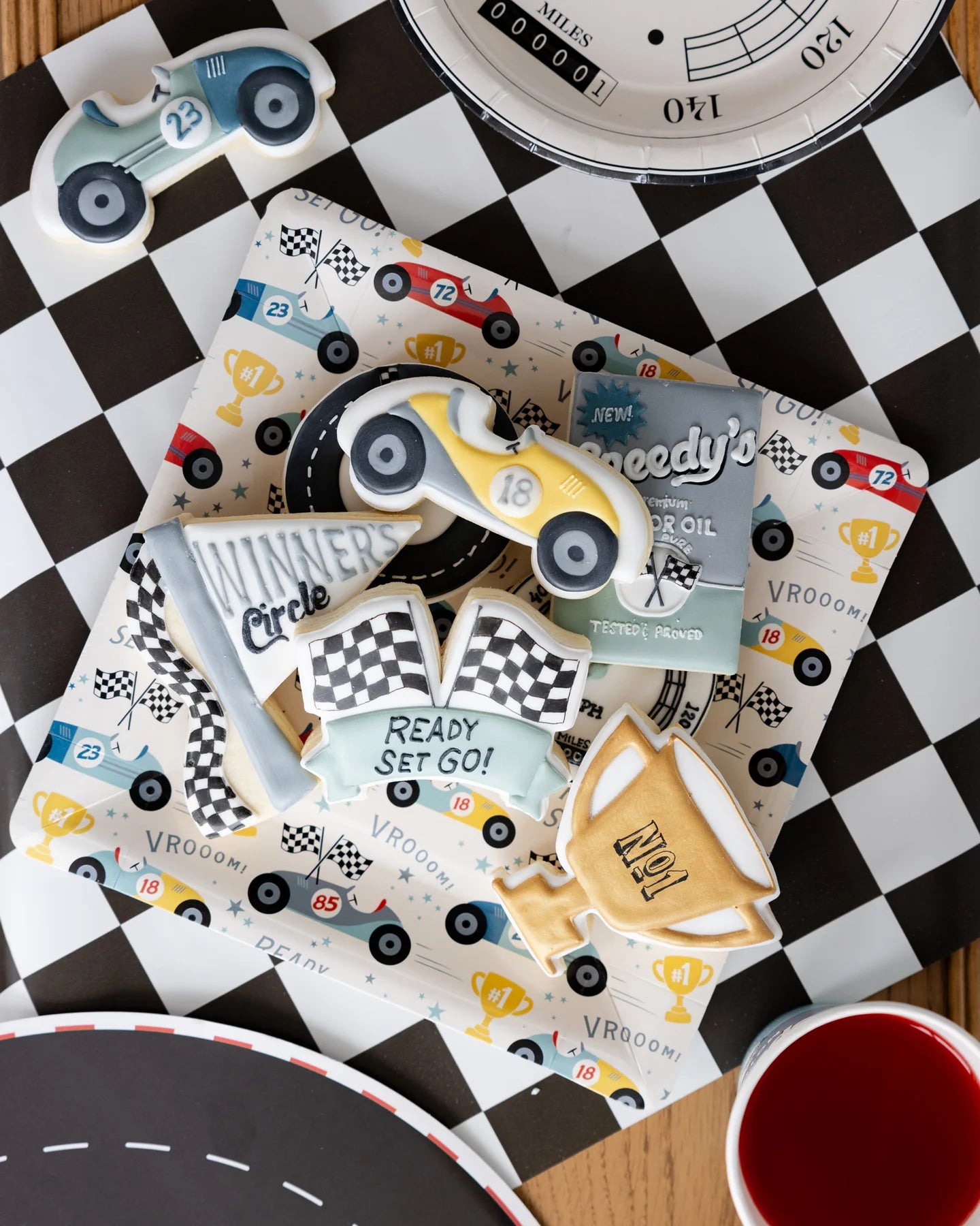 Race car-themed paper plate with scattered colourful vintage race car icons, topped with race car-themed sugar cookies