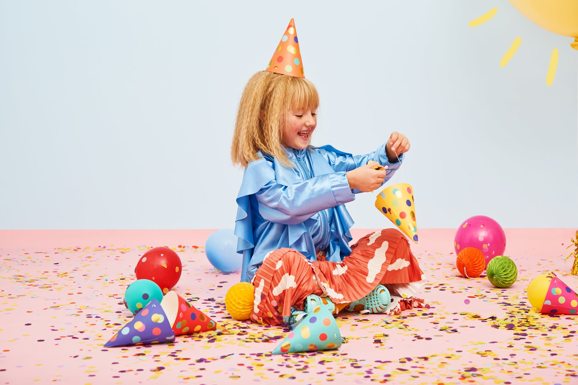 young girl wearing party hat sitting on confetti covered floor