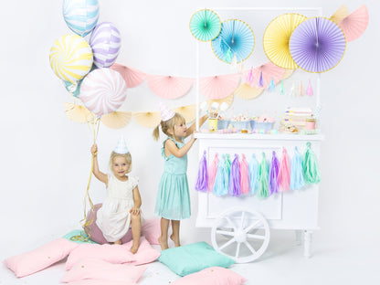 A sweet cart display with pastel party supplies and two young girls, one holding balloons.