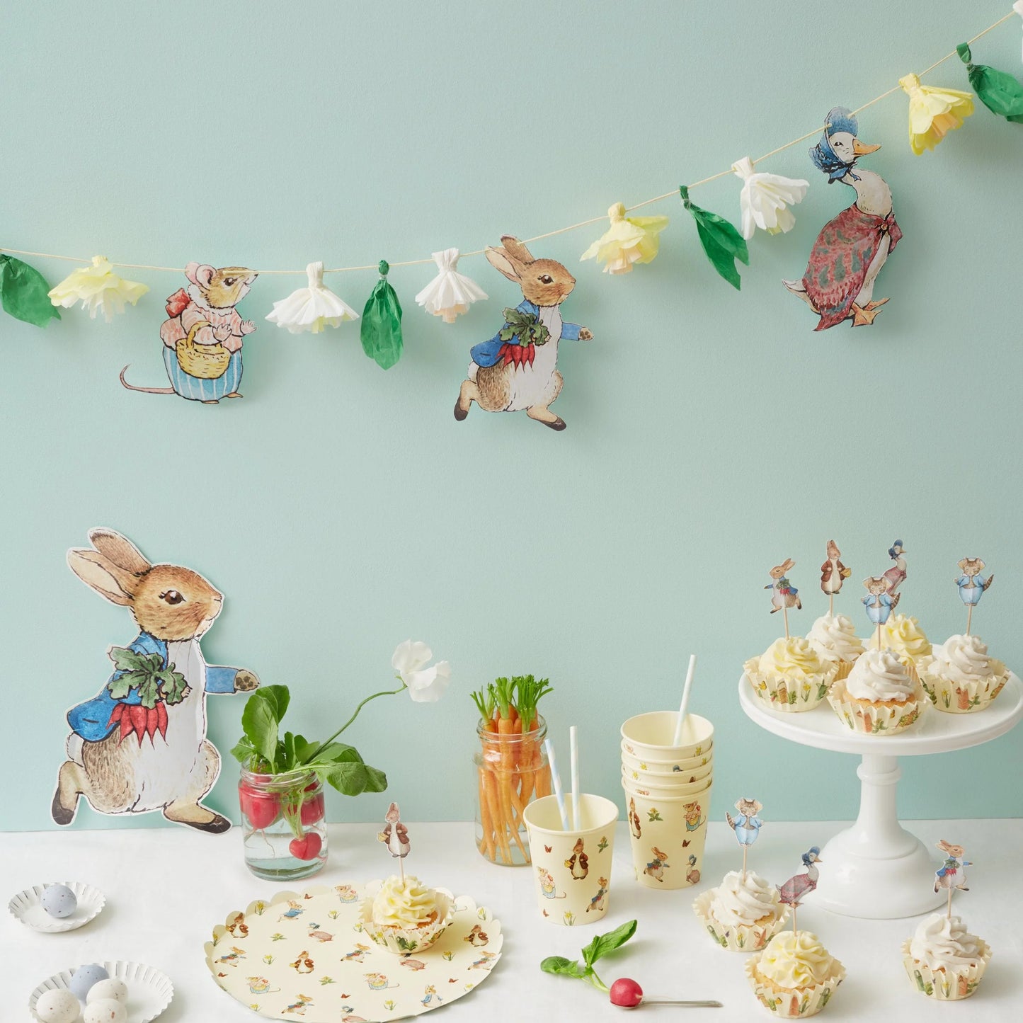 peter rabbit themed birthday party table with cupcakes, party decorations and a hanging garland