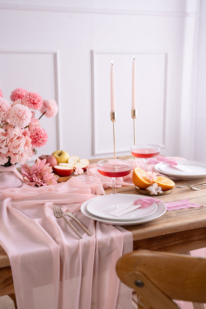 pink chifforn table runner with matching table candles, flowers and plate setting.