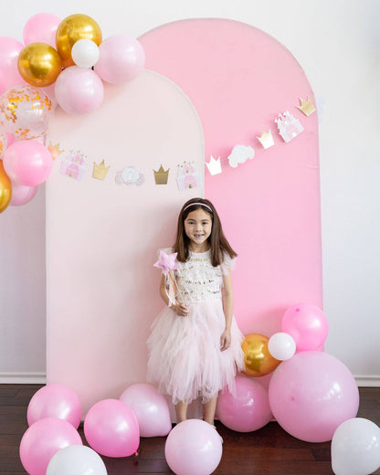 girl standing in front of a balloon arch backdrop with princess decor 