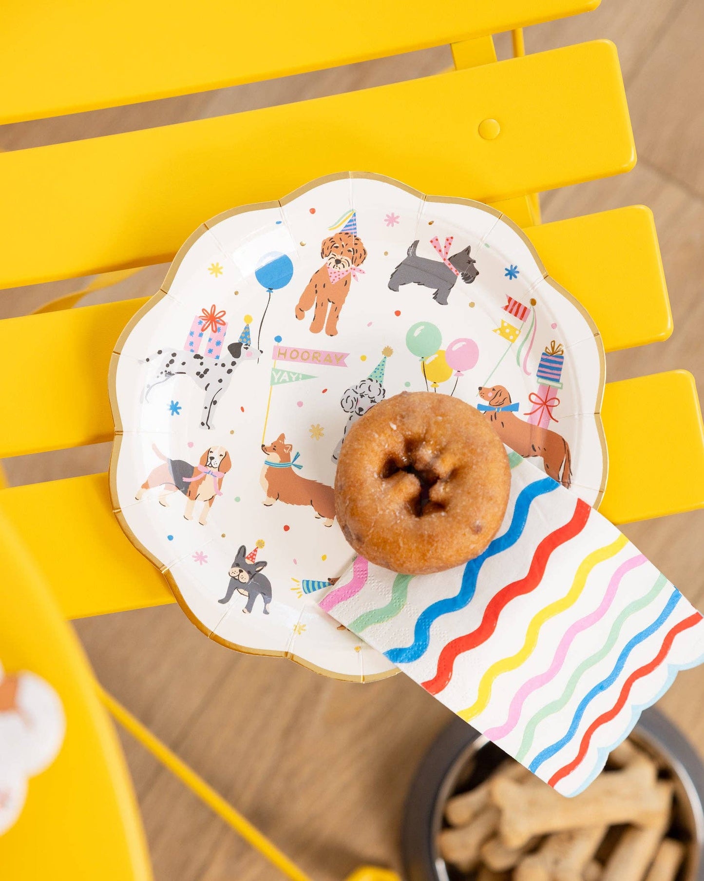 donut placed on a puppy icon paper plate with colourful wavy striped dinner napkin+ dog treats 