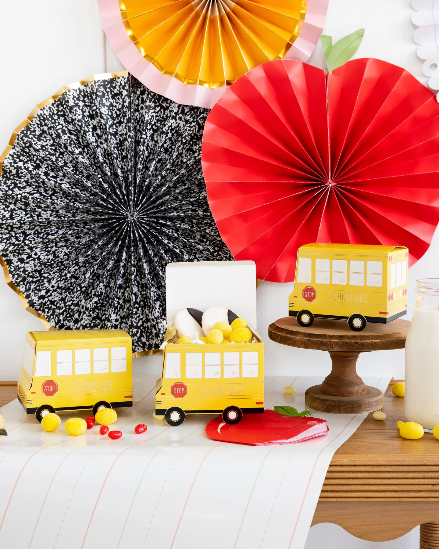 Back-to-school themed table setup with 3 school bus shaped treat boxes and colourful paper fans on wall.