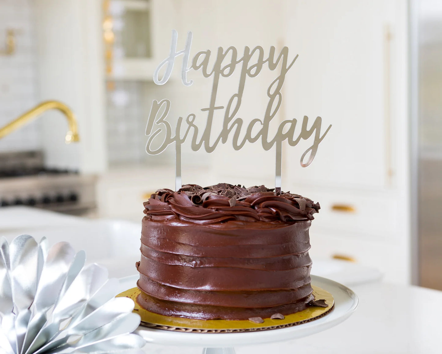 chocolate frosted cake with silver acrylic 'happy birthday' cake topper