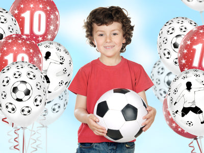 boy holding a soccer ball surrounded by soccer themed helium balloons