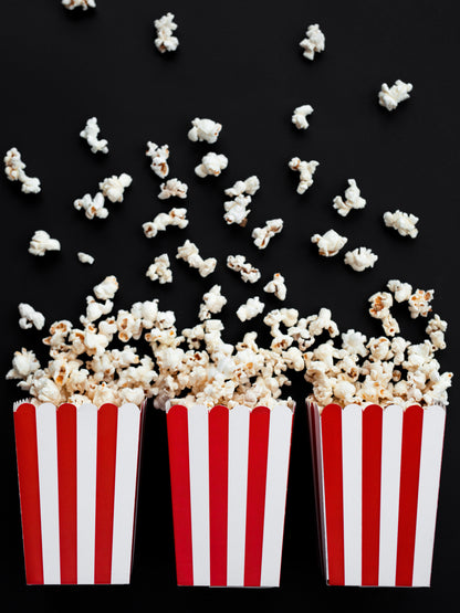 flat lay photo of 3 red and white striped popcorn boxes with popcorn spilling