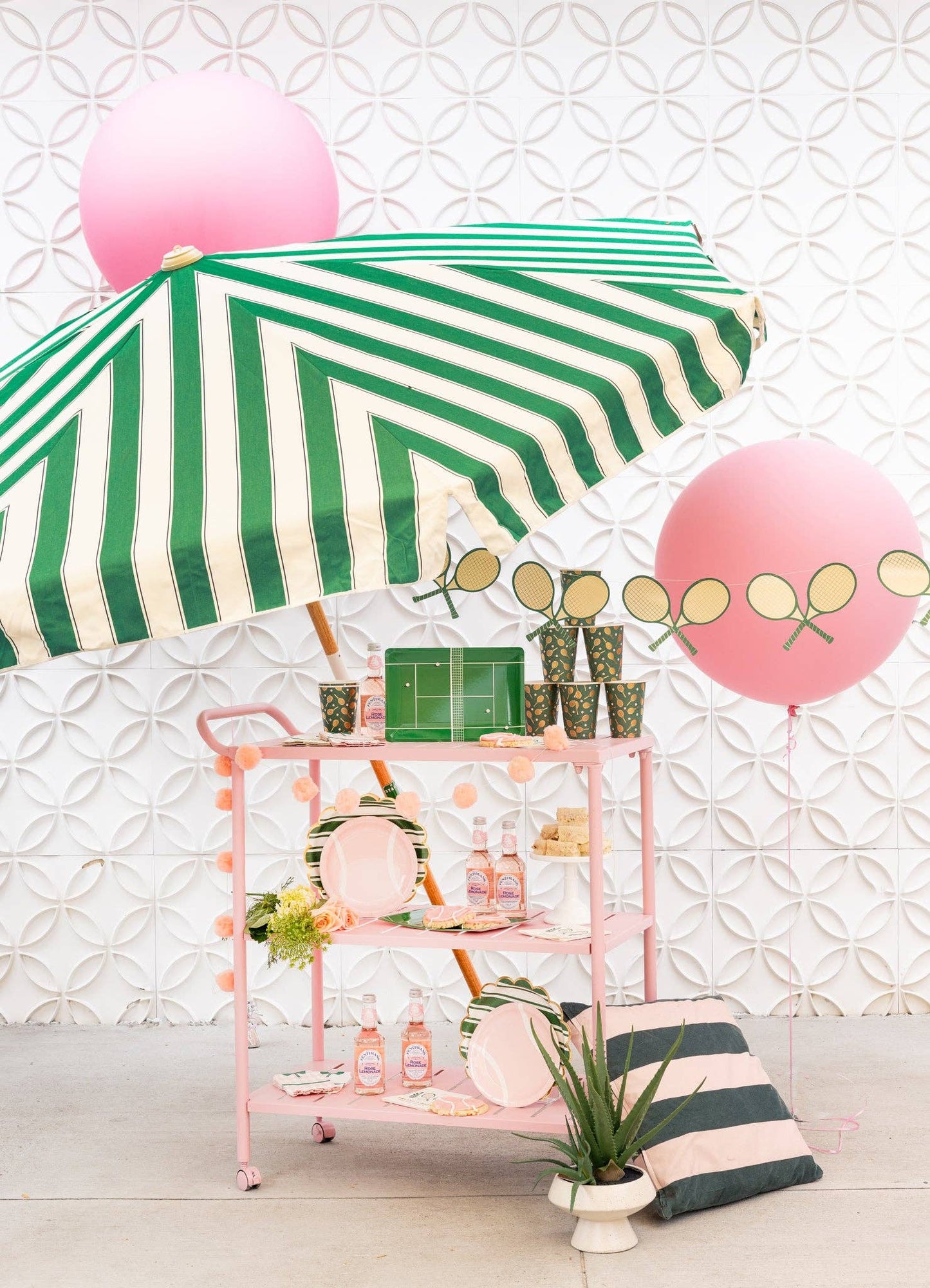 tennis party setup with all the tennis collection under a striped umbrella and pink balloon