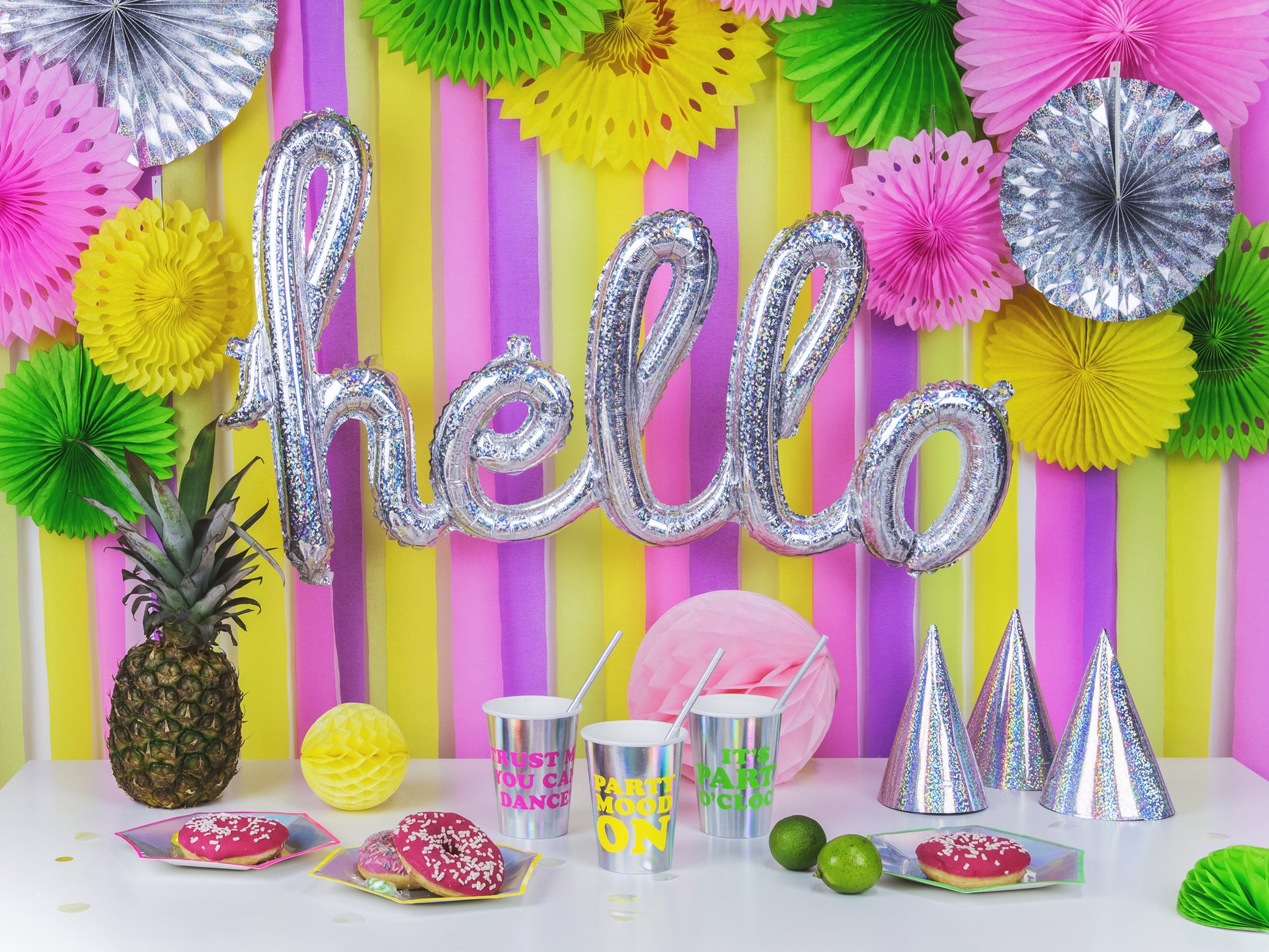 Tropical-themed party setup with pineapples, yellow, pink, and green paper fans, and streamers.