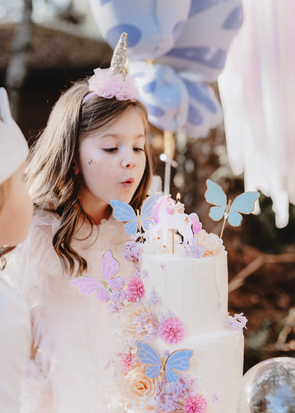 unicorn themed birthday cake with girl blowing out unicorn candle 