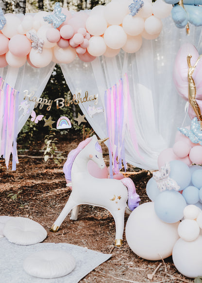 unicorn themed balloons, backdrop and hanging happy birthday banner 